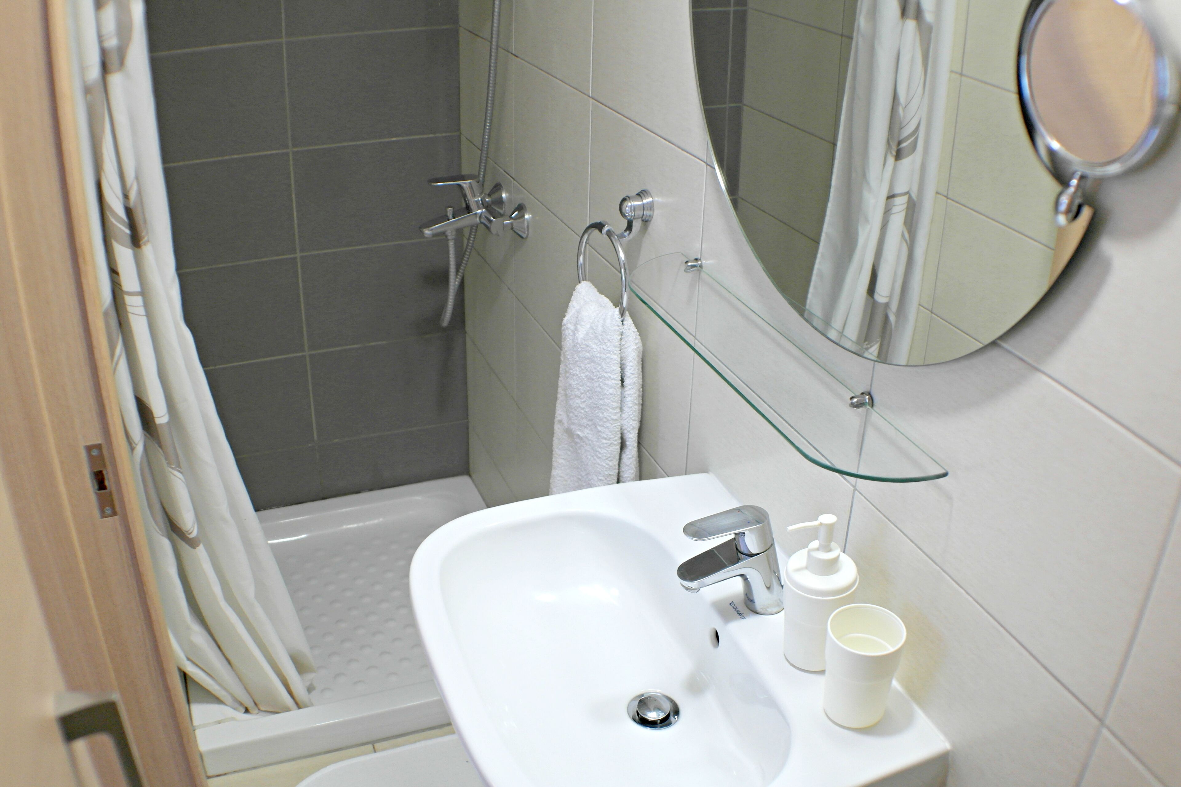 A bathroom with a white sink, a glass shelf, a handheld showerhead, and a mirror.