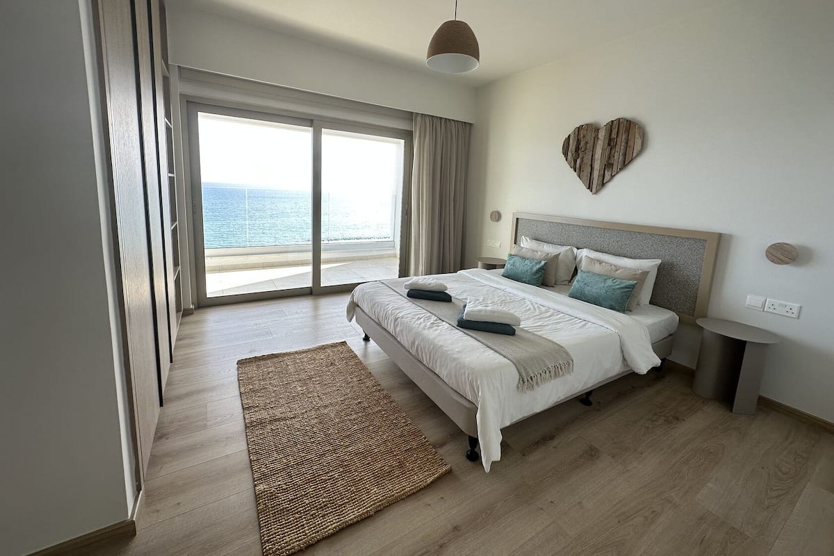 A bedroom with a large bed, a view of the sea, and a wooden floor.