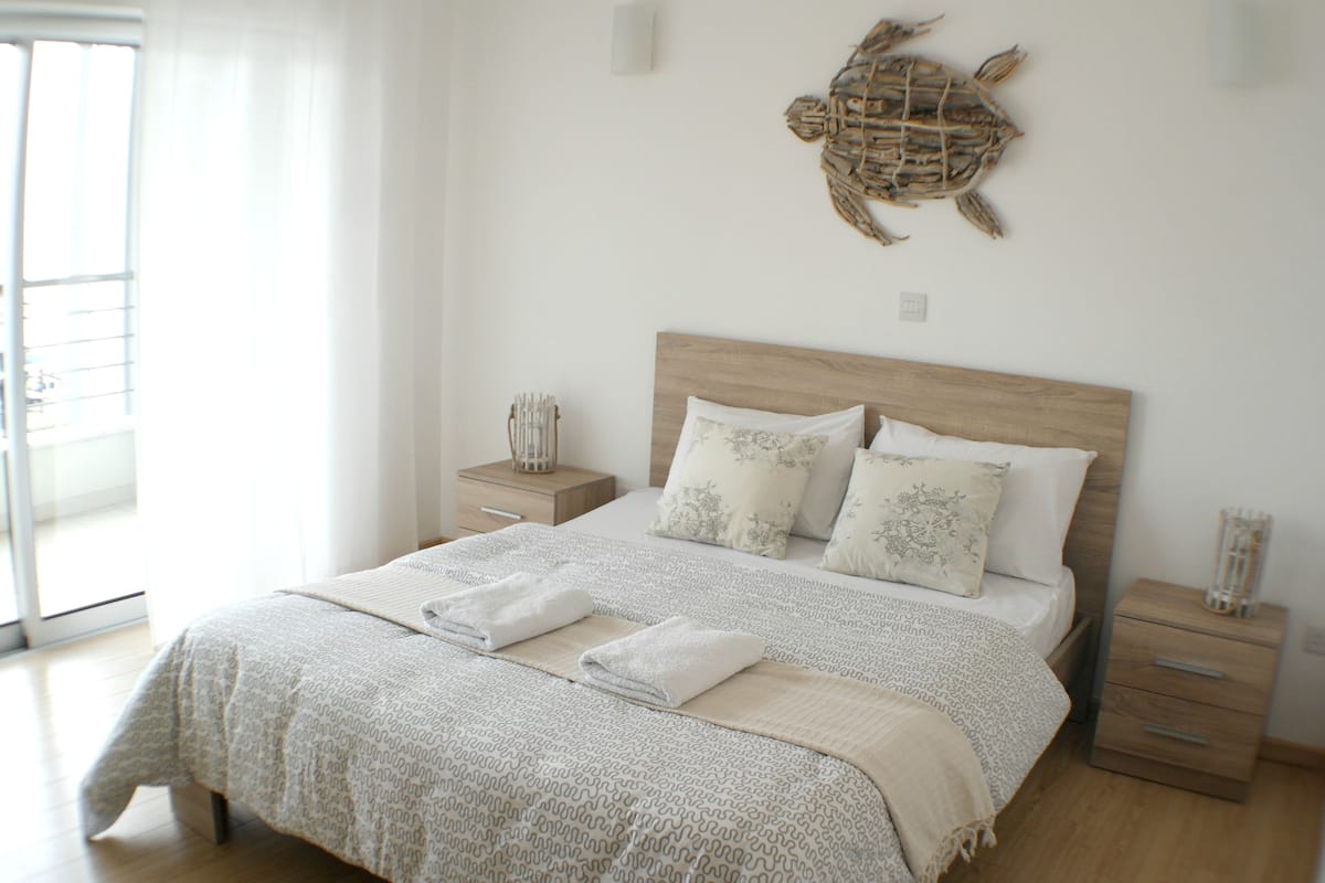 A bedroom with a wooden headboard, a large bed with patterned bedding, two bedside tables, and a decorative turtle on the wall.