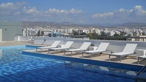 A rooftop pool with lounge chairs and a cityscape view in the background.