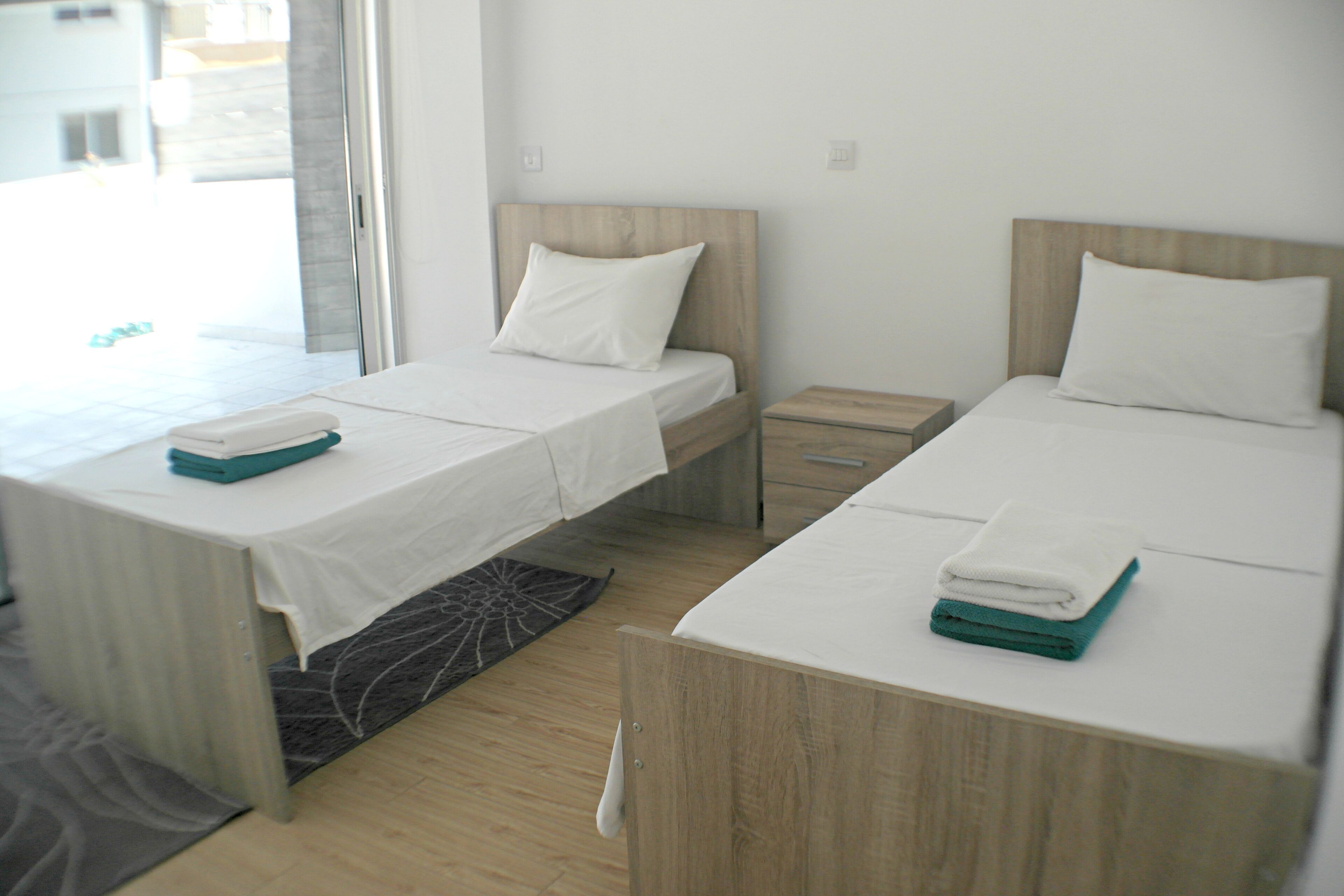 A hotel room with two beds, a small wooden nightstand, and a window providing a view of the outside.