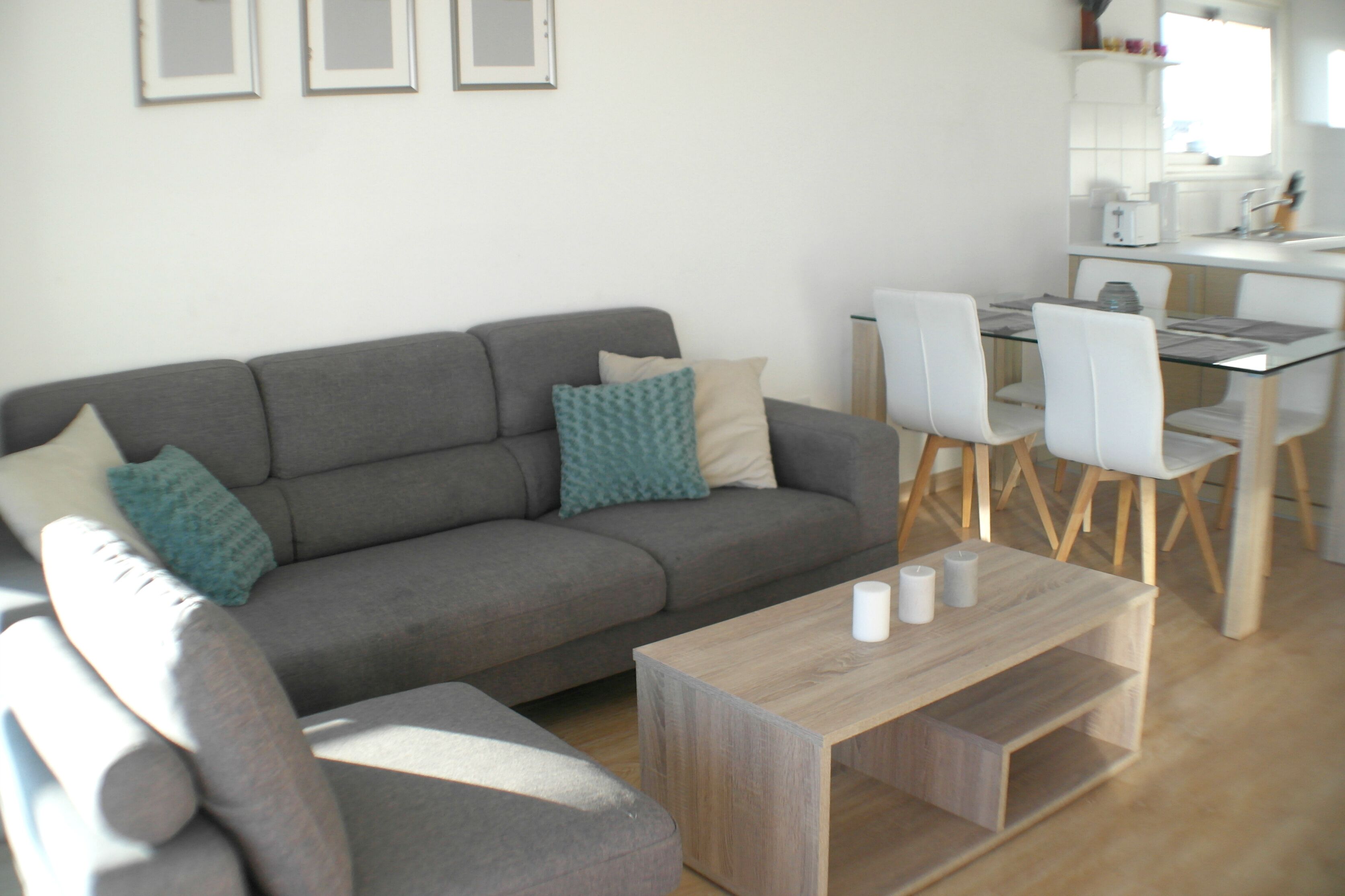 A modern living room with a grey sofa, a glass coffee table, and white chairs.