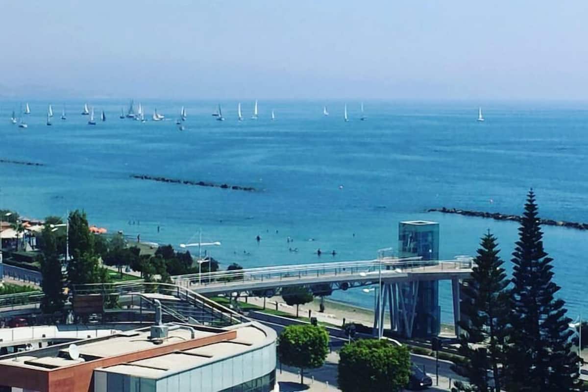 A coastal cityscape with a modern bridge, sailboats on the water, and a clear view of the sea.