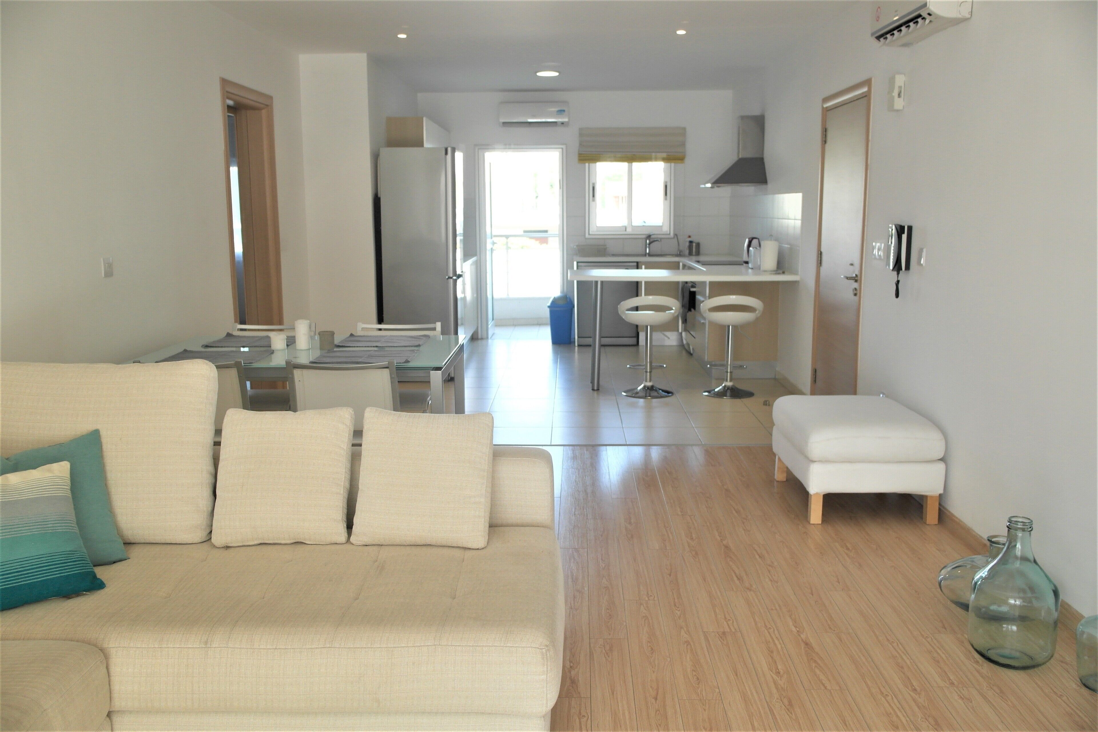 Uma sala de estar moderna com um sofá, um banquinho pequeno e um espaço de jantar com mesa e cadeiras.