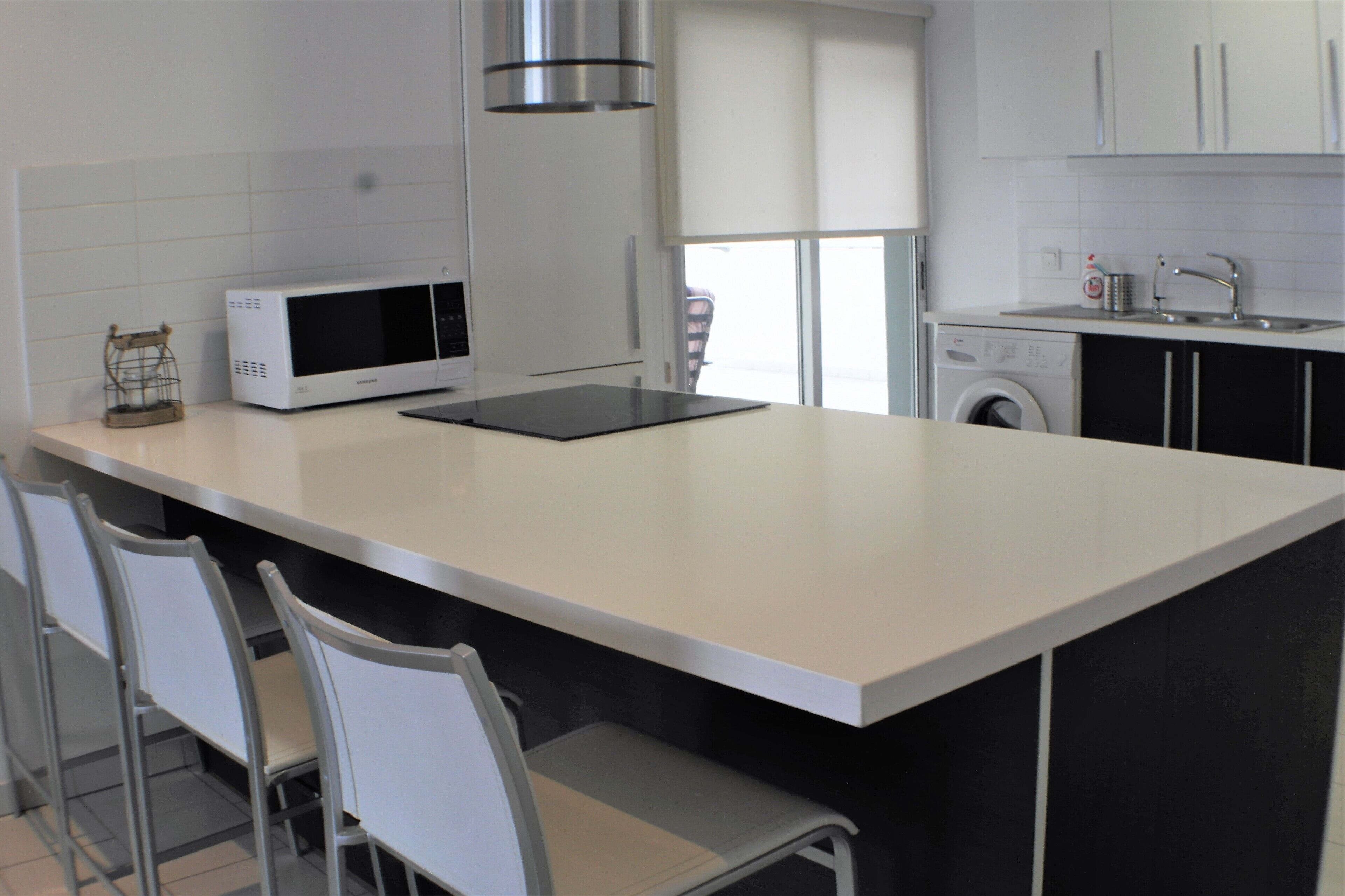 Una cucina moderna con una grande isola, un forno a microonde, una lavatrice e sgabelli da bar.