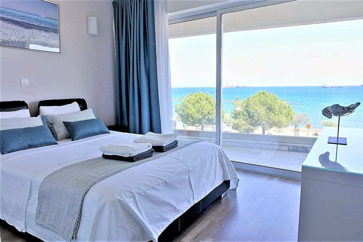 A modern hotel room with a large bed, a view of the sea, and a balcony with a chair.