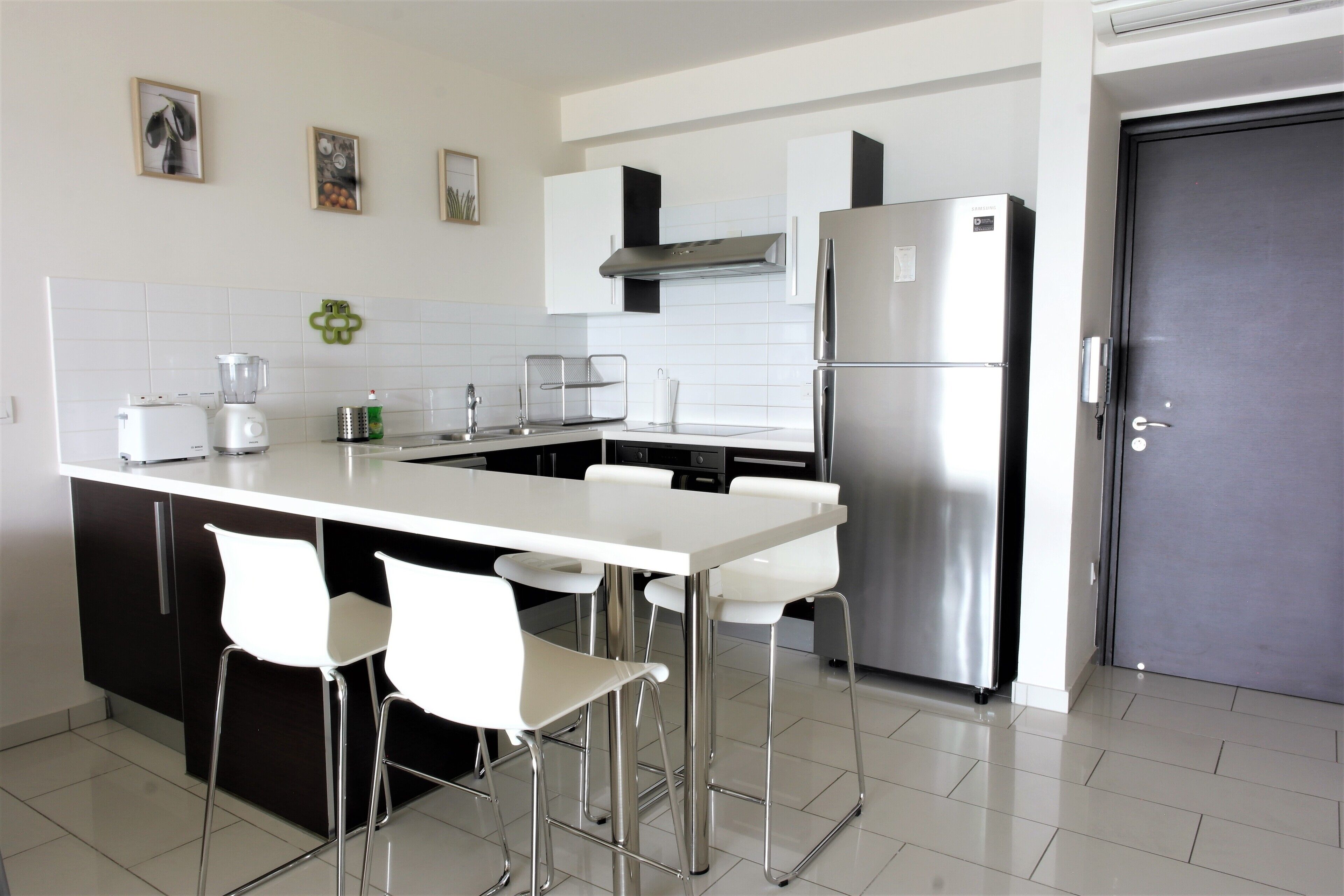 Una cocina moderna con una isla central, electrodomésticos de acero inoxidable y taburetes blancos.