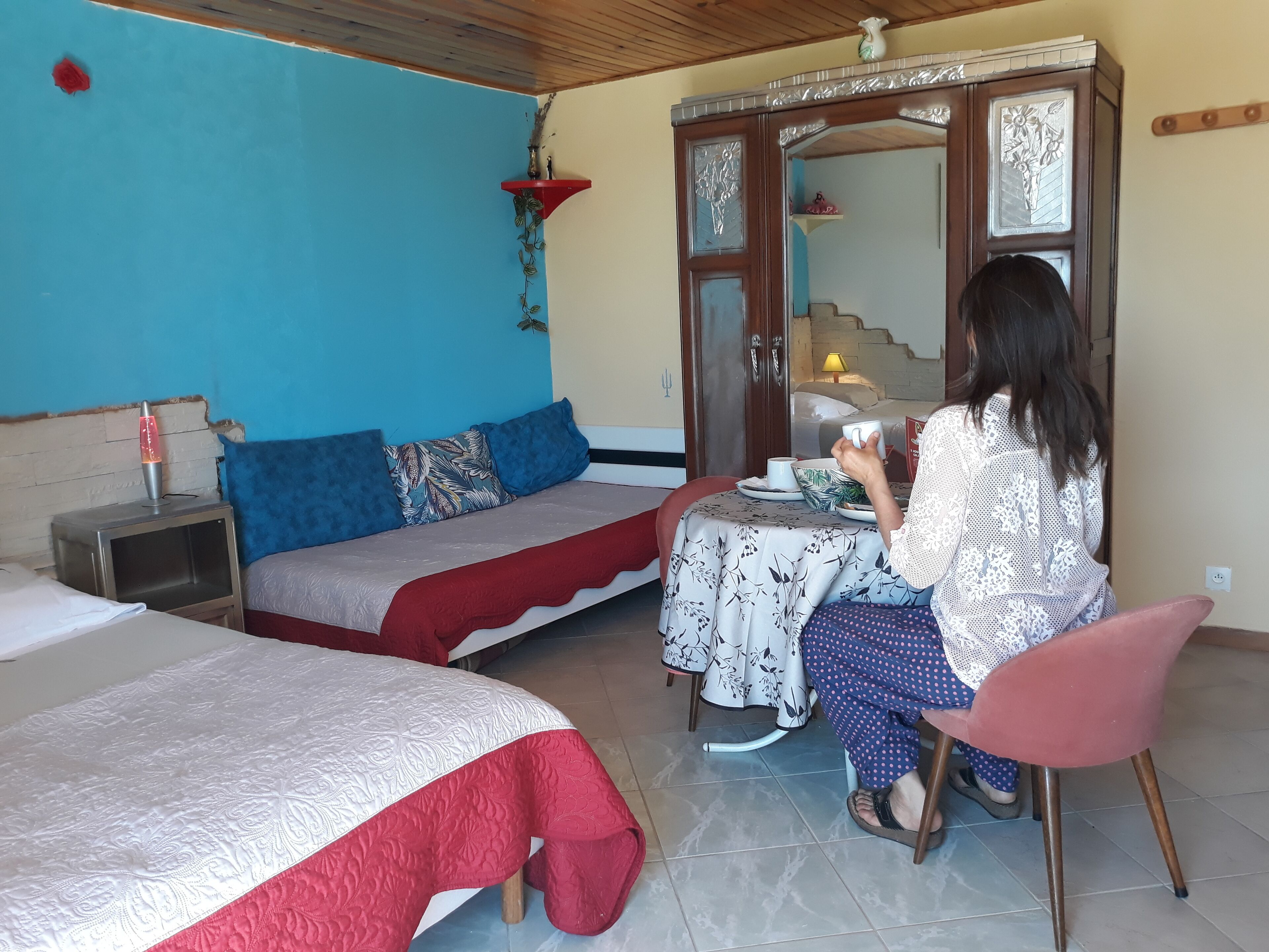 Une pièce comprenant un lit, une table recouverte d’une nappe, une chaise et un miroir.