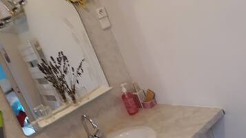 Un baño con un lavabo blanco, un espejo y un estante pequeño con artículos de aseo.