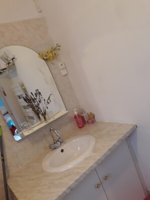 Un baño con un lavabo blanco, un espejo y un estante pequeño con artículos de aseo.