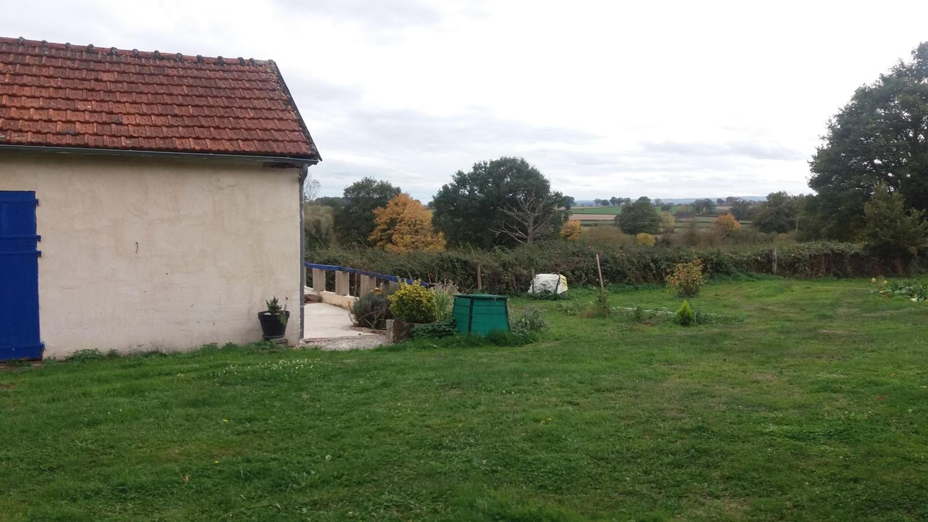 Una propiedad rural con una casa pequeña, un patio cercado y un cobertizo verde.