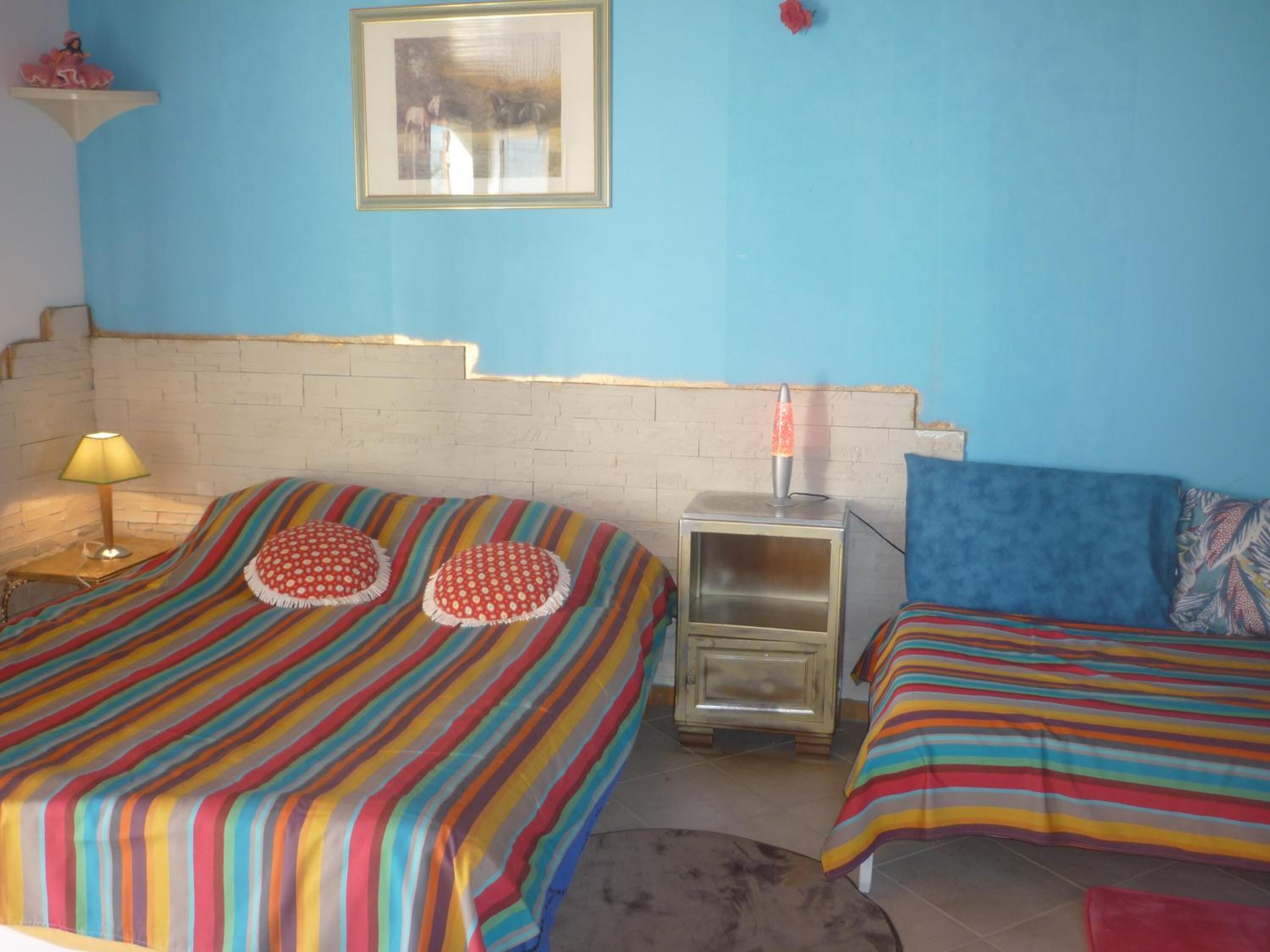 Una habitación con dos camas, cada una con ropa de cama a rayas y una mesita con una lámpara de lava.