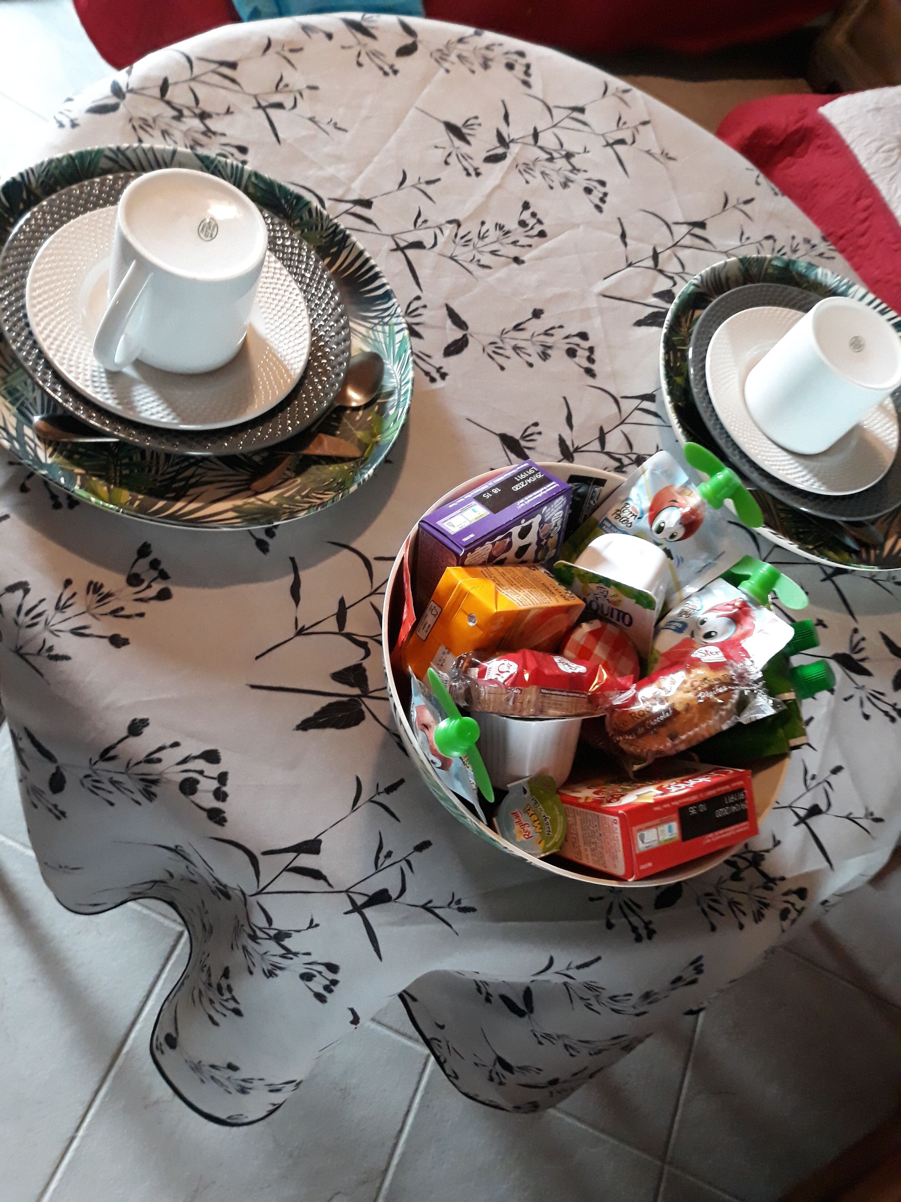 Una mesa con mantel floreado, dos platos con tazas y un bol de aperitivos variados.