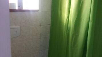 Un baño con cortina de ducha verde, un inodoro con asiento de madera y una ventana sobre el inodoro.