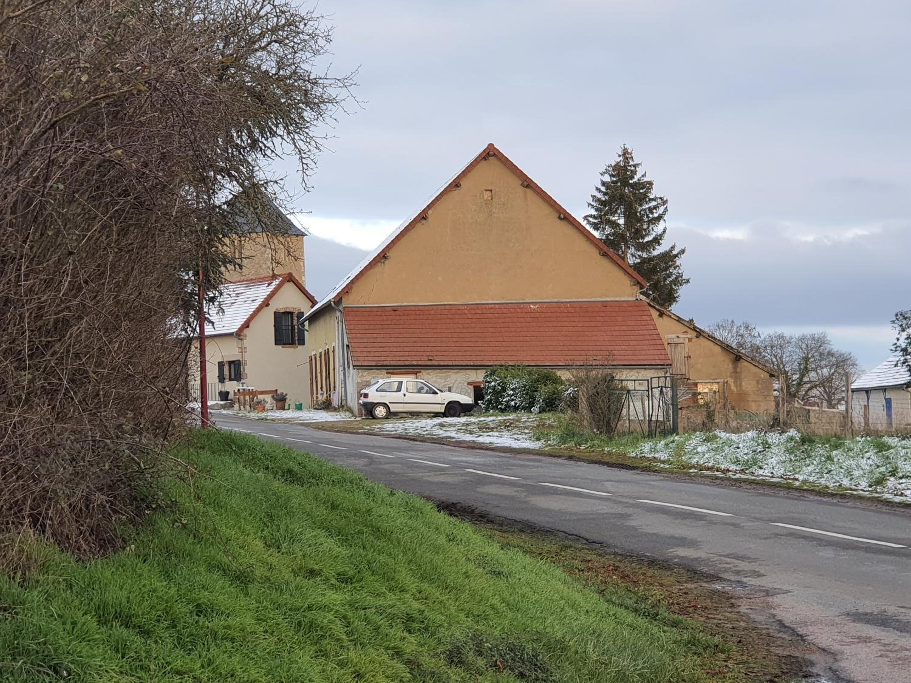 Un camino rural con un edificio de una sola planta, techo inclinado y un coche estacionado.