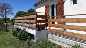 Un bâtiment blanc avec un toit recouvert de tuiles rouges, des volets en bois et des fondations en béton.