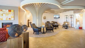 A modern lobby with a unique curved ceiling light fixture, comfortable seating, and a fireplace. - Dünenmeer Ferienhäuser (Ostseebad Dierhagen)
