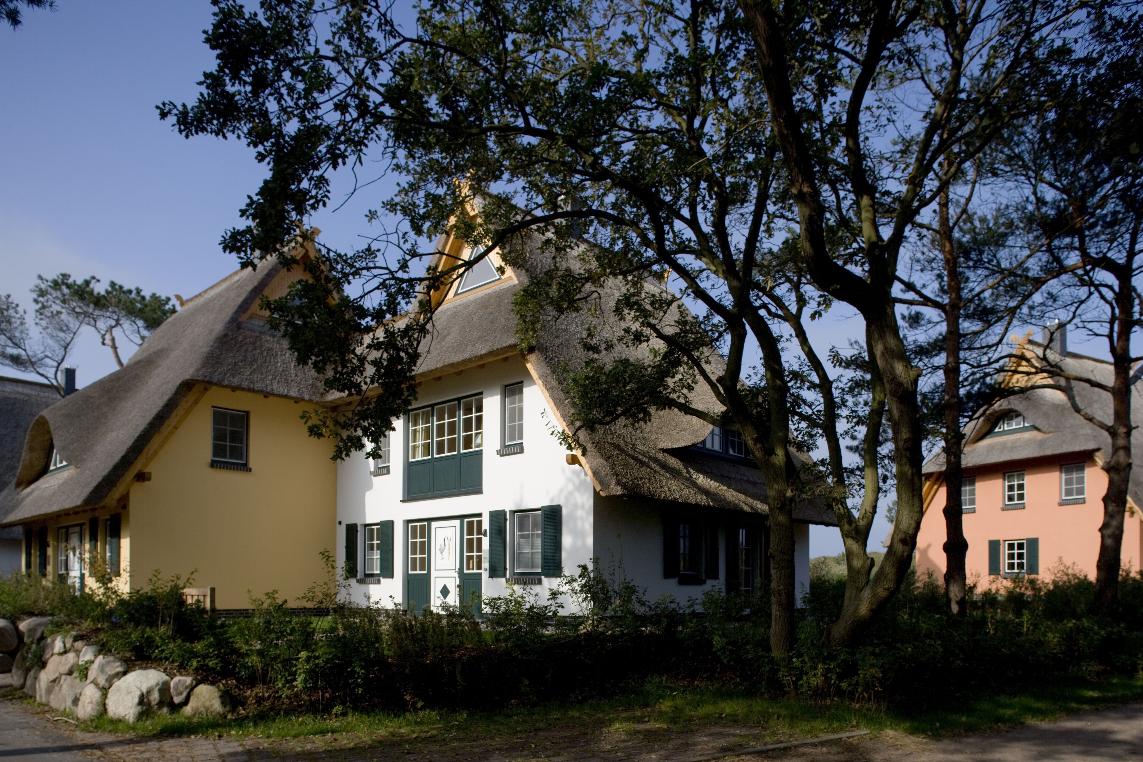 Ein traditionelles Haus mit Strohdach, weißen Wänden und grünen Fensterläden.