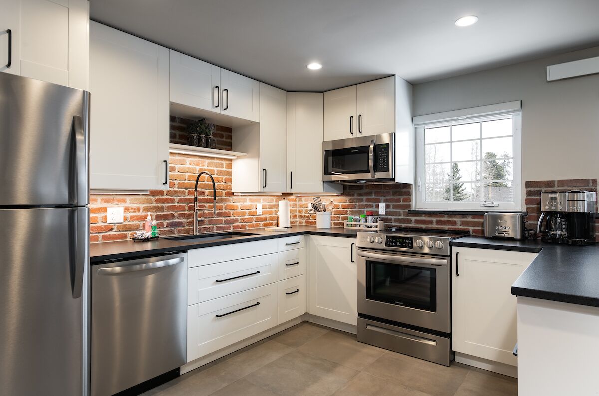 Una cocina moderna con electrodomésticos de acero inoxidable, armarios blancos y una pared decorativa de ladrillo.