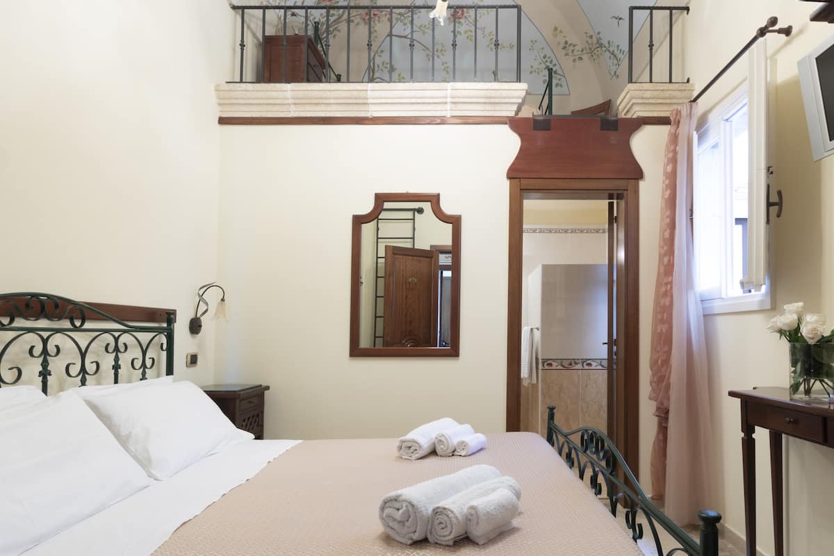 Une chambre à coucher avec un lit, un miroir, une fenêtre avec des rideaux et un balcon.