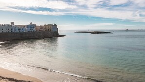 Vista costeira com edifícios ao longo da praia, águas calmas e um farol ao longe.