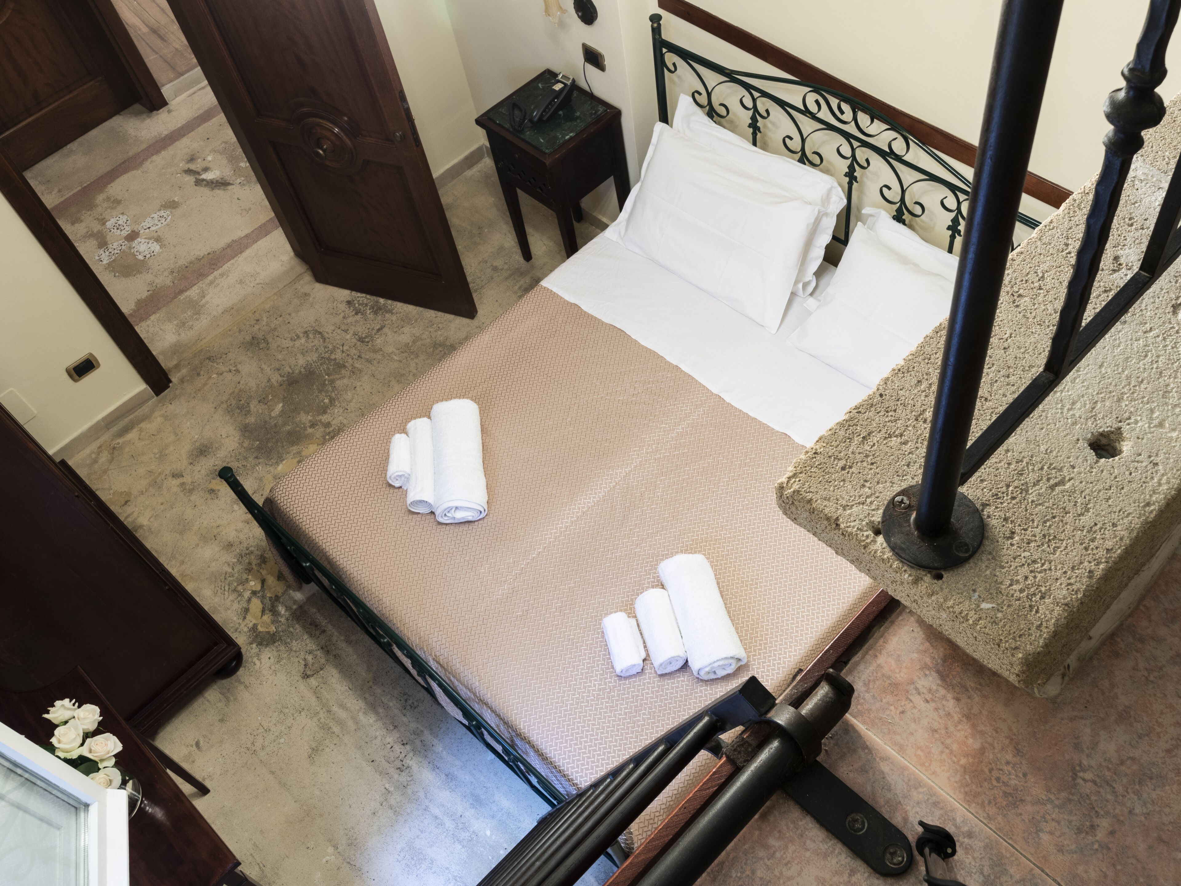 A hotel room with a bed, a nightstand, a telephone, and a view of the hallway.