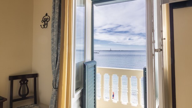 Quarto com vista para o mar, uma cadeira de madeira e uma varanda com corrimão.