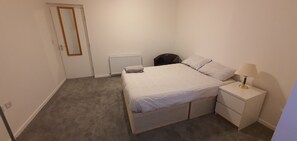 A bedroom with a single bed, a bedside table with a lamp, a radiator, and a door. - Livingstone 2 (Ashford)