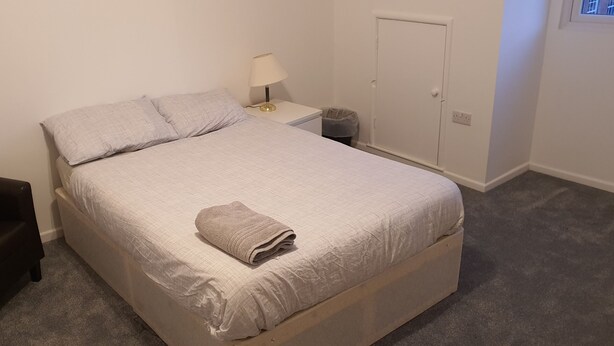 Une chambre à coucher comprenant un lit, une table de chevet, une lampe, une chaise et une armoire.