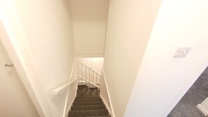 Un escalier étroit, aux murs blancs, avec des marches recouvertes de moquette et des rampes blanches.