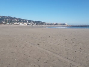 Una extensa playa de arena con una vista despejada del océano y un horizonte urbano distante.