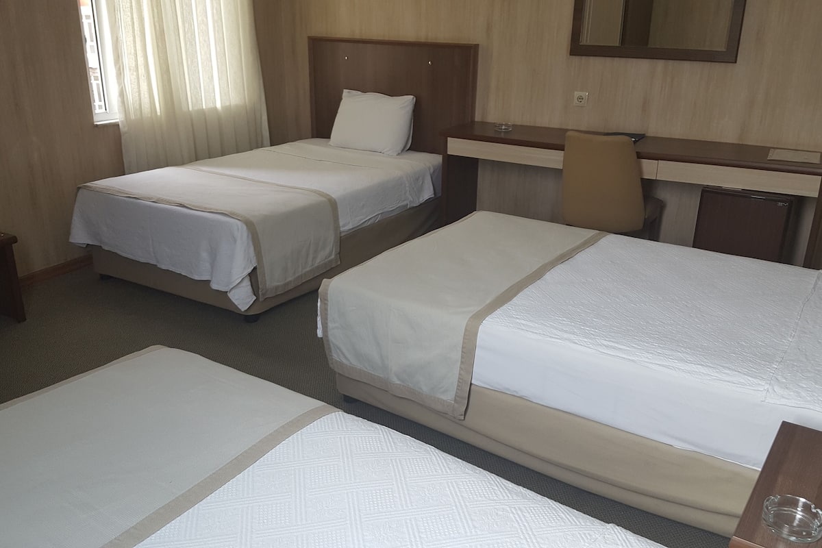 A hotel room with three beds, a desk, a chair, and a small table.