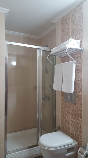 A bathroom with a glass-enclosed shower, a toilet, and a towel rack with two towels. - Hosta Otel (Adana)