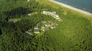 Luchtbeeld van een resort met meerdere gebouwen, een strand en dicht bos.