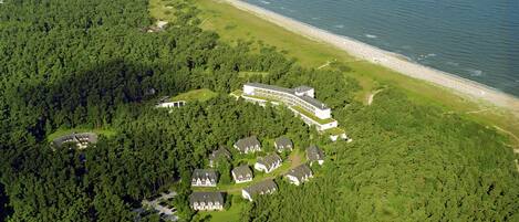 An aerial view of a resort with multiple buildings, a beach, and dense forest.