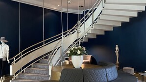 Een modern interieur met een spiraaltrap, een ronde zwarte bank, een klein rond tafeltje en een witte sculptuur.