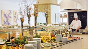 Een buffetopstelling met diverse gerechten en voedingsmiddelen, een kok in uniform en decoratieve elementen zoals vazen en wanddecoratie.