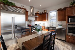 A modern kitchen with stainless steel appliances, wooden cabinets, and a dining area with a table and chairs. - Modern Apartment directly across from Lake Michigan (Grand Haven)