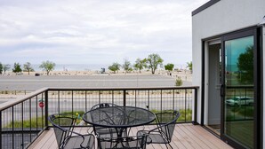 Un balcón con mesa y sillas, con vistas a un estacionamiento y a la playa.