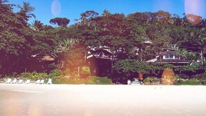 A beach with a row of white lounge chairs and a building with a sloped roof. - Pousada Terral Surf (Itacaré)