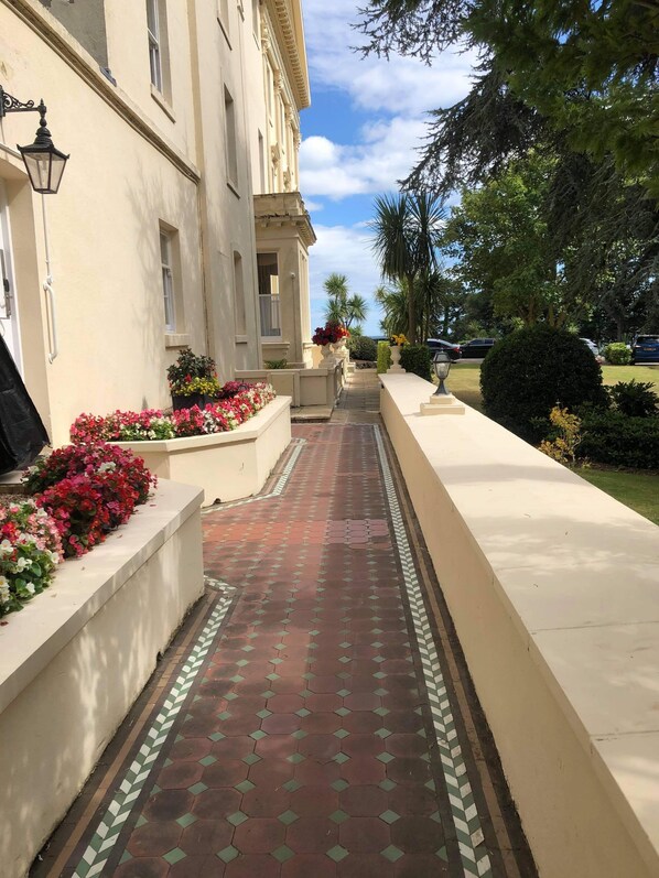 A pathway lined with flower beds and a building with classical architecture. - ***Graciously large one bed by the Sea*** (Torquay)