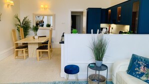 Ein modernes Wohnzimmer mit Essbereich, einem weißen Sofa, einem blauen Teppich und einer Küche mit dunkelblauen Schränken.