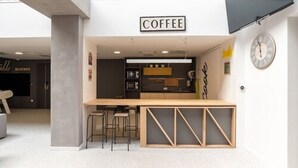 Ein modernes Café mit minimalistischem Design, das eine zentrale Bar und Stehtische sowie ein Schild mit dem Schriftzug "COFFEE" zeigt.
