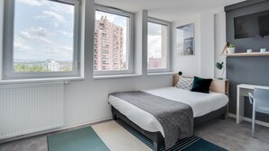 Ein modernes Schlafzimmer mit Bett, Schreibtisch und großen Fenstern mit Blick auf die Stadt.