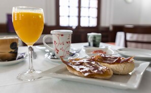 Une table mise pour le petit-déjeuner avec un verre de jus d’orange, une tasse à motifs floraux et une assiette contenant des toasts et du jambon.
