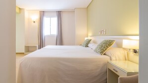 A hotel room with two beds, a bedside table, a chair, and a window with curtains. - Hotel Platería by Bossh Hotels (Ecija)