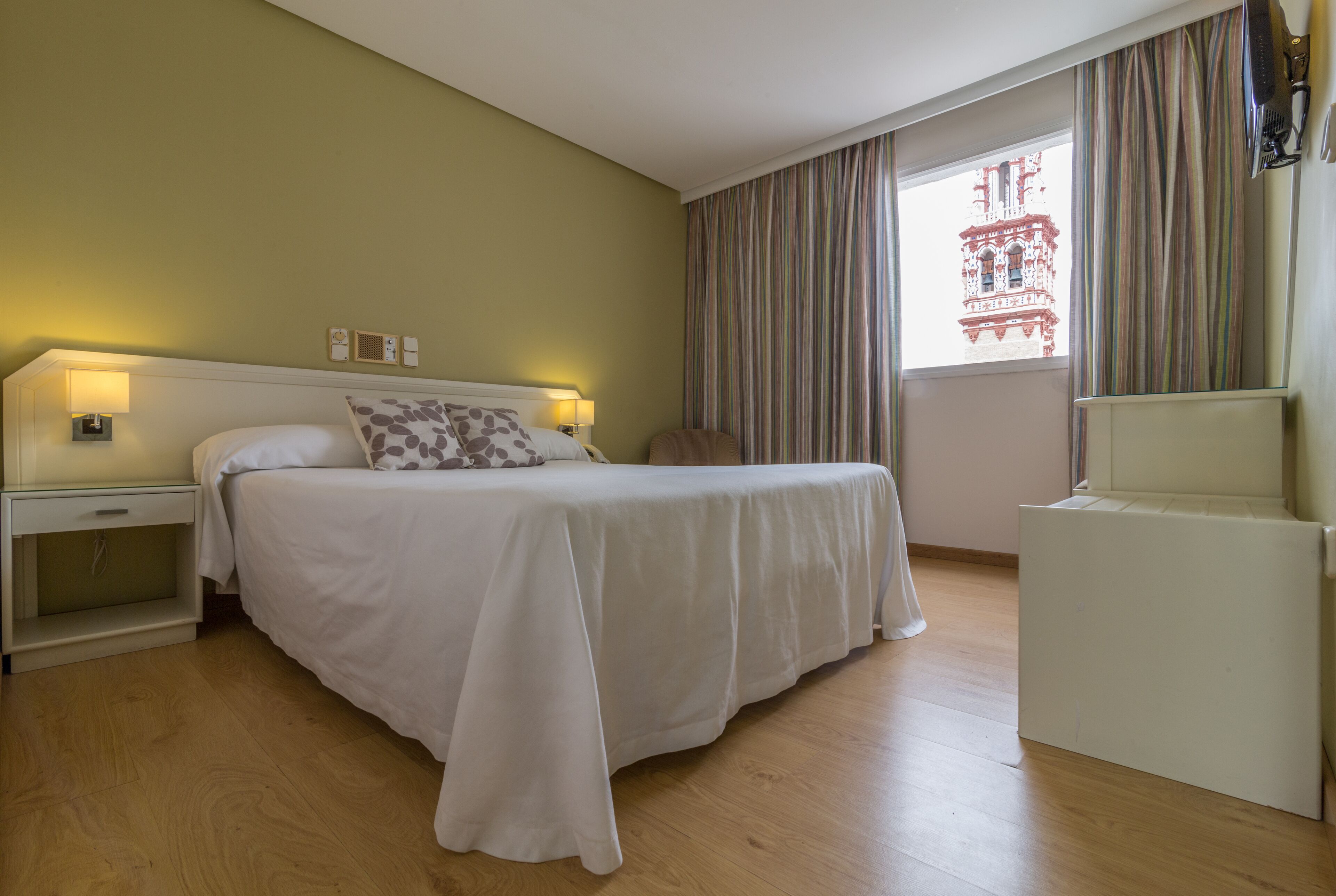 Una habitación de hotel con una cama, mesitas de noche, un escritorio y una ventana con cortinas.