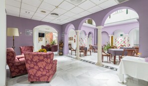 Een hotellobby met paarse wanden, een betegelde vloer en een zithoek met sofa’s en tafels met bloemenprint.