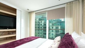 A modern hotel room with a large bed, a TV, and a view of a cityscape through a large window. - River view Luxury 3bed flat with views (London)