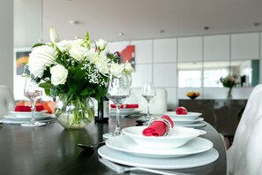 Une table à manger dressée avec de l’argenterie blanche, des verres et un vase rempli de fleurs blanches.